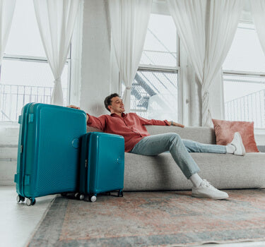 man sitting on sofa comfortably with luggage beside