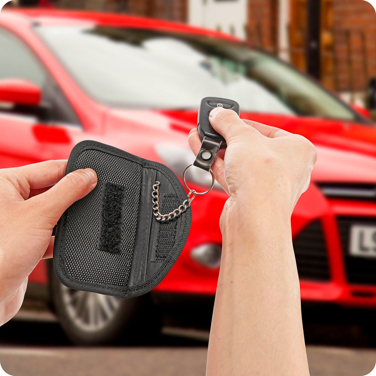 Image showing two hand holding product in black and aiming key fob at red car in the background.